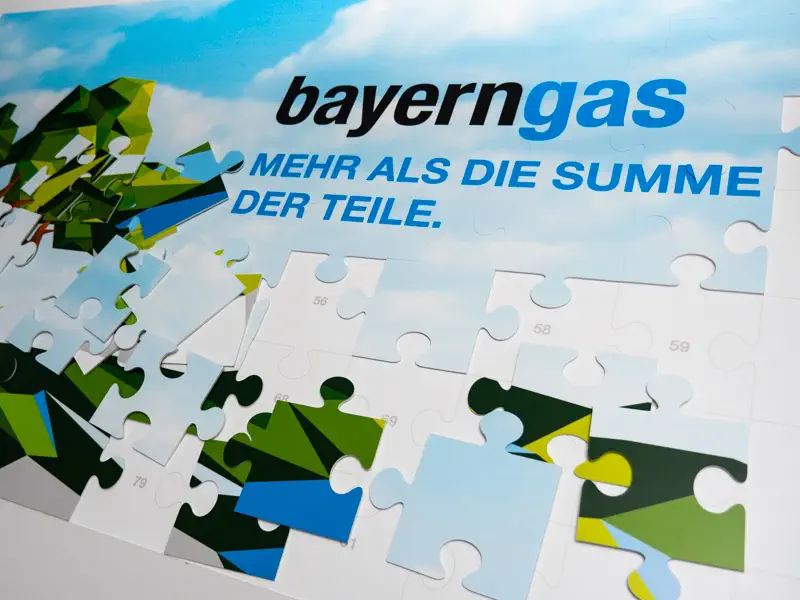 Unvollständiges Puzzle mit einem Motiv aus stilisierten Bäumen und blauem Himmel, gestaltet im Rahmen eines Corporate Designs durch eine Corporate Design Agentur. Das Bayerngas-Logo ist oben zu sehen, begleitet vom Slogan 'MEHR ALS DIE SUMME DER TEILE.' in blauer Schrift.

Mehrere Puzzleteile fehlen noch, wodurch Teile des Bildes und des Textes unterbrochen sind – eine visuelle Metapher für strategische Markenentwicklung und die Bedeutung eines durchdachten Corporate Designs für eine vollständige und kohärente Markenidentität.