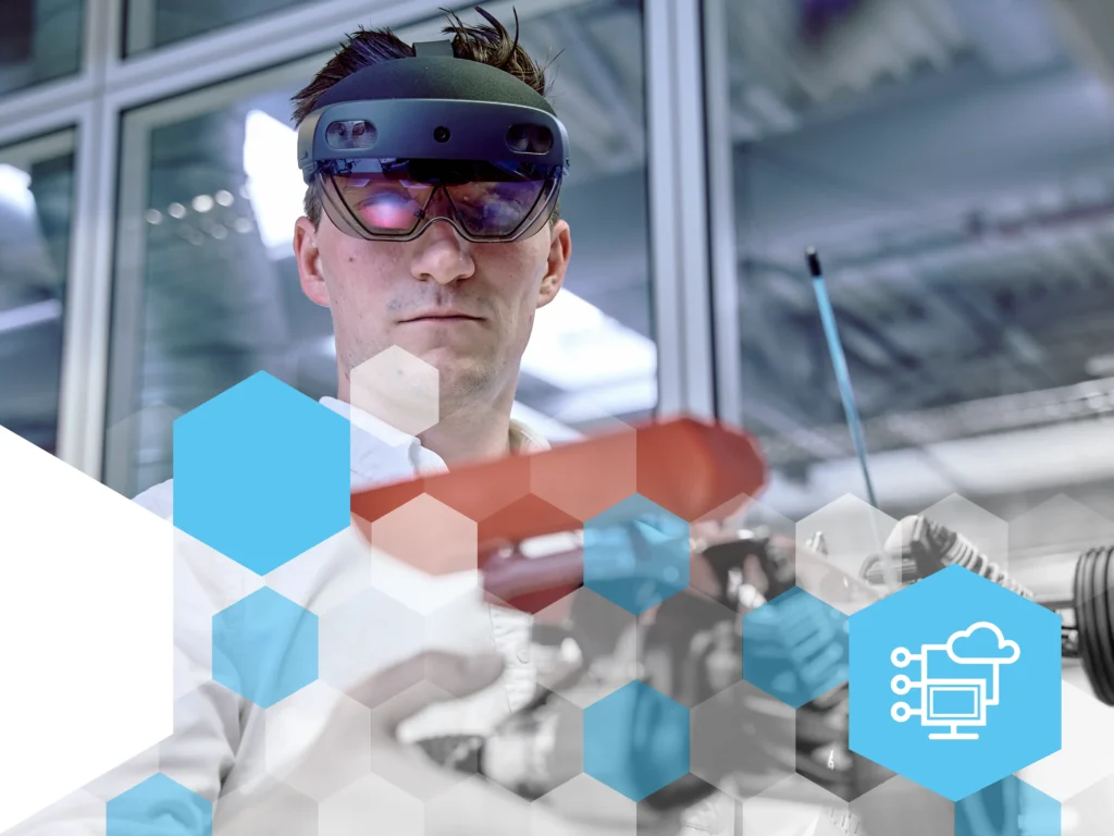 Ein Mann mit einer Augmented-Reality-Brille arbeitet konzentriert an einem Modellfahrzeug in einer modernen Industrieumgebung. Er trägt ein weisses Hemd und hält ein Bauteil mit einer roten Abdeckung. Im Hintergrund sind Glaswände und industrielle Strukturen sichtbar. Die Bildgestaltung enthält überlagerte blaue hexagonale Designelemente, unten rechts befindet sich ein blaues Hexagon mit einem weissen Symbol für Digitalisierung.