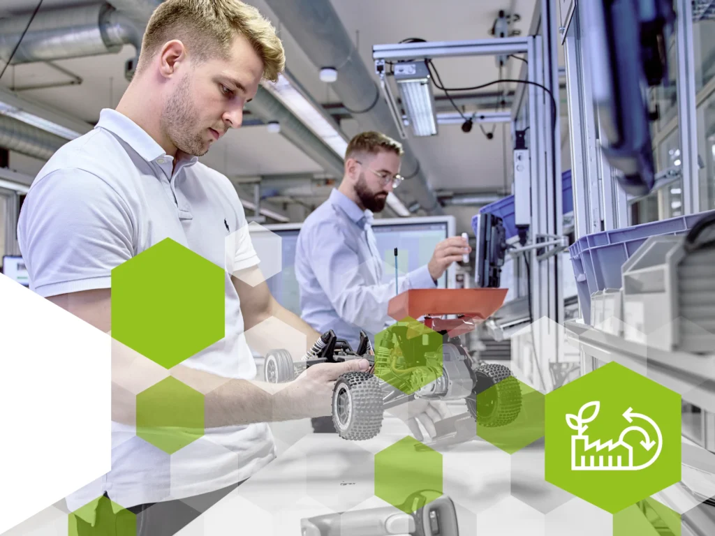 Zwei Männer in einem modernen Industrieumfeld arbeiten an einem Modellfahrzeug. Der Mann im Vordergrund trägt ein weisses Polo-Shirt und montiert ein Rad an das Fahrzeug, während der Mann im Hintergrund in einem hellblauen Hemd einen Bauteil aus einem Behälter entnimmt. Die Arbeitsplätze sind mit Monitoren und blauen Lagerboxen ausgestattet. Überlagert sind grüne hexagonale Designelemente, unten rechts befindet sich ein grünes Hexagon mit einem weissen Symbol für Kreislaufwirtschaft.