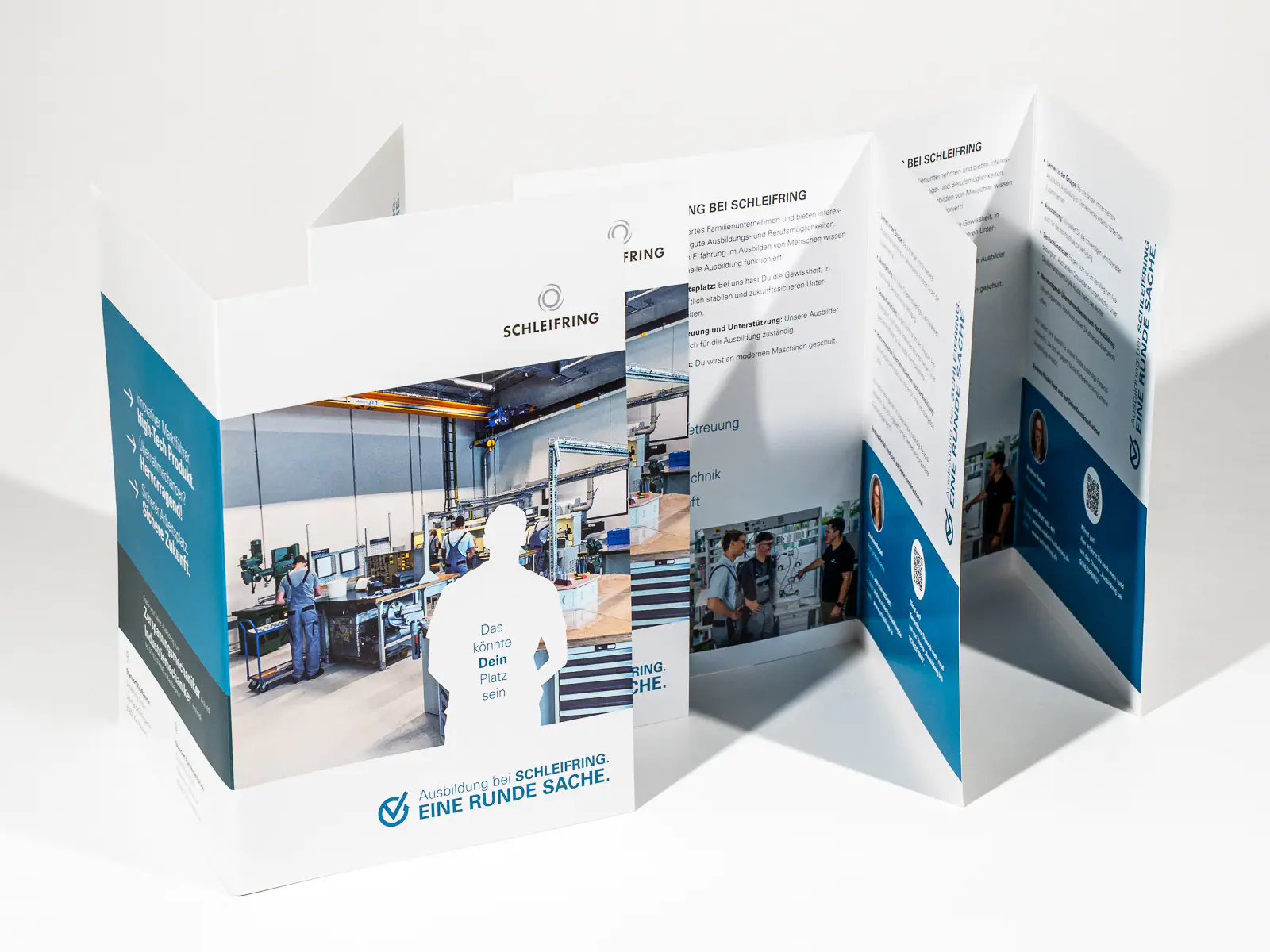 Mehrseitiger, aufgestellter Faltprospekt der Firma SCHLEIFRING zum Thema Ausbildung. Die Titelseite zeigt ein Bild einer Produktionshalle mit arbeitenden Personen, wobei eine weisse Silhouette mit der Aufschrift „Das könnte Dein Platz sein“ eingefügt wurde. Darunter steht der Slogan „Ausbildung bei SCHLEIFRING. EINE RUNDE SACHE.“ Die aufgeklappten Seiten enthalten Informationen über die Ausbildung, Vorteile sowie Bilder von Auszubildenden und Betreuern. Das Design nutzt Blau- und Weiss­töne mit strukturierten Textabschnitten und QR-Codes.