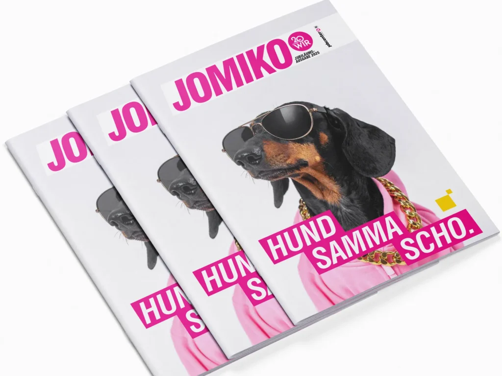 Three overlapping copies of the magazine “JOMIKO”. The cover features a dachshund wearing sunglasses, a pink top and gold chains, alongside the headline “Hund samma scho.”.