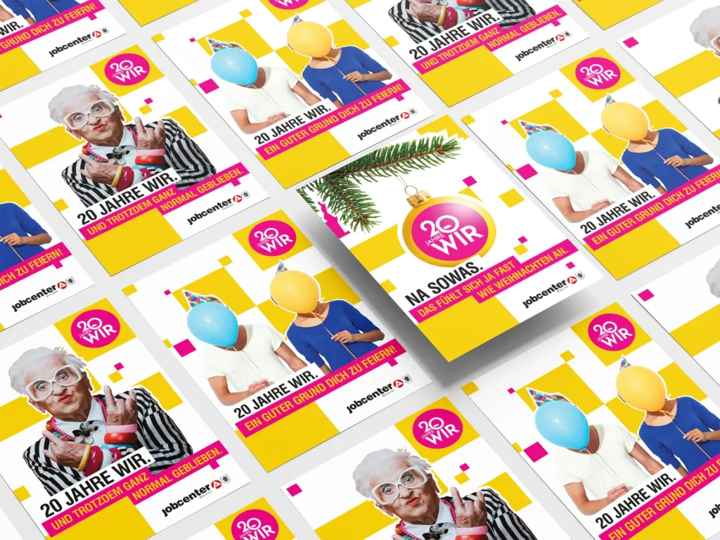 Perspective view of several anniversary posters for Jobcenter München. The designs feature people with balloons, an older woman and, in the centre, a Christmas bauble bearing the words “20 Jahre WIR”.